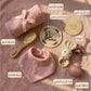 Collection of baby care items including a hat, brush, and toys on a soft pink background.